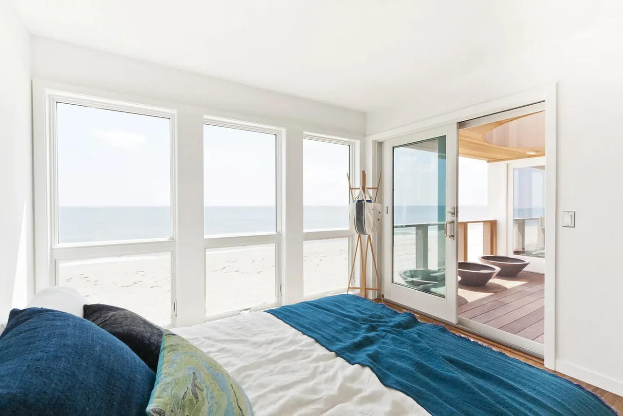 Bedroom with wide horizontal windows and sliding glass door offering beachfront ocean views in the Dune Road Beach House.