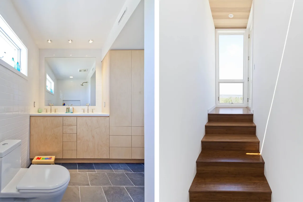 Bathroom with wood vanity and tiled floor next to a staircase with natural wood steps and a window above.