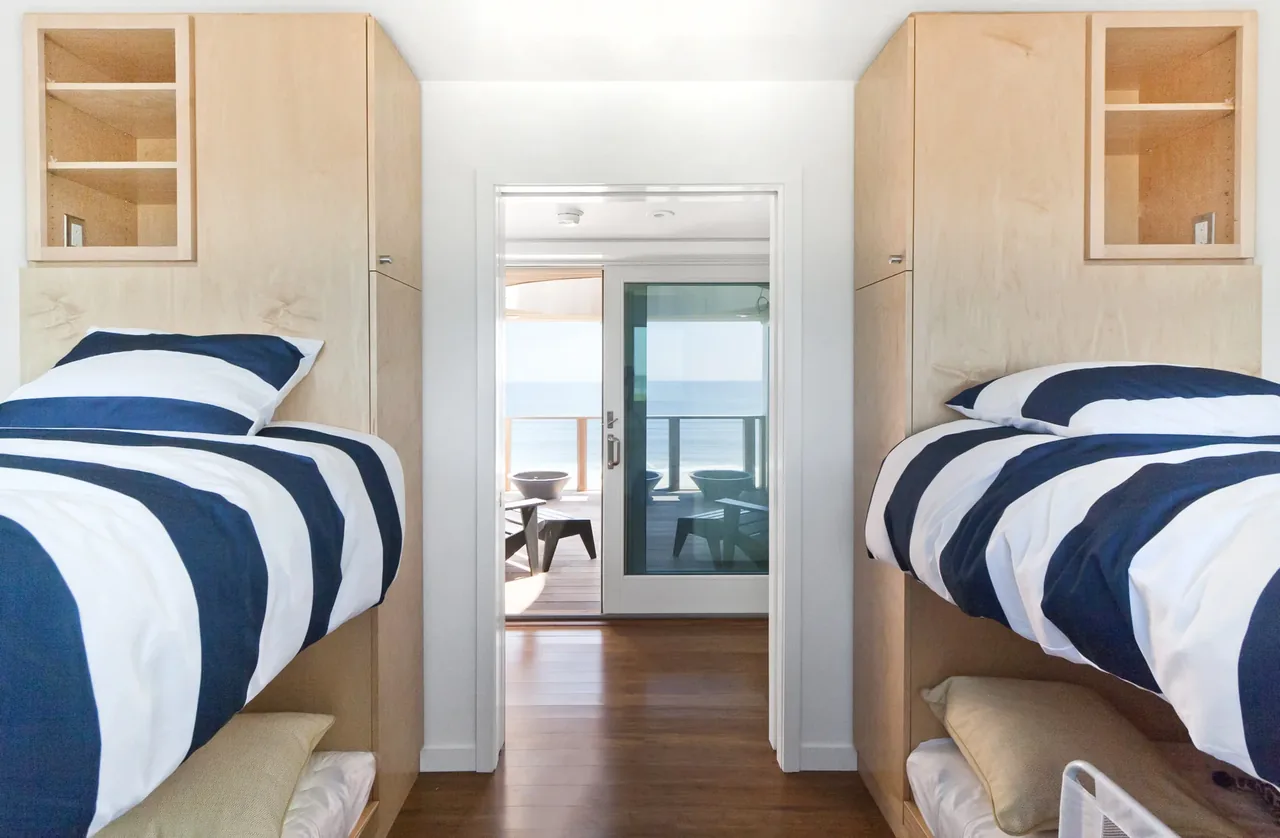 Bedroom with built-in plywood bunk beds overlooking the ocean through a sliding glass door.