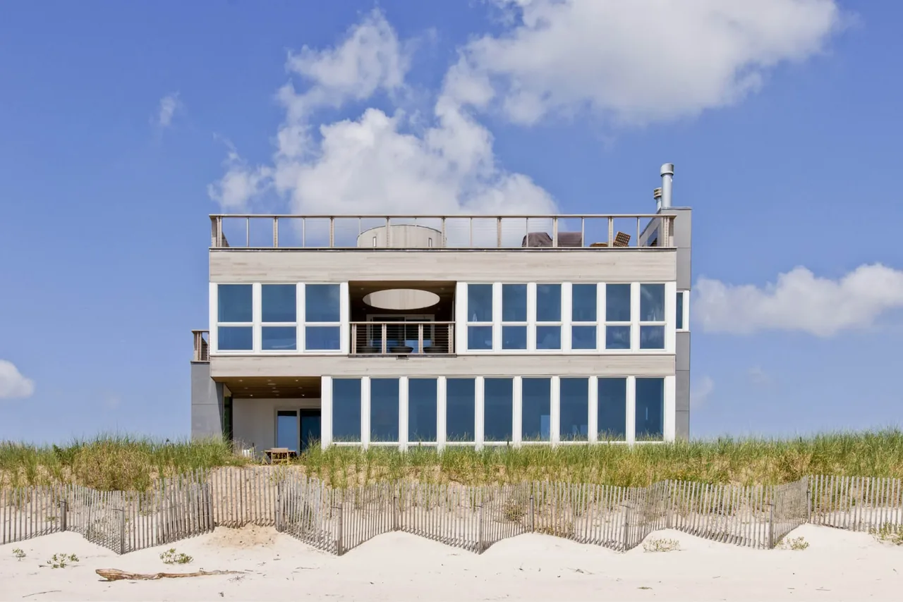 Dune Road Beach House in East Quogue, NY with wide horizontal windows and a rooftop deck designed by Resolution 4 Architecture.
