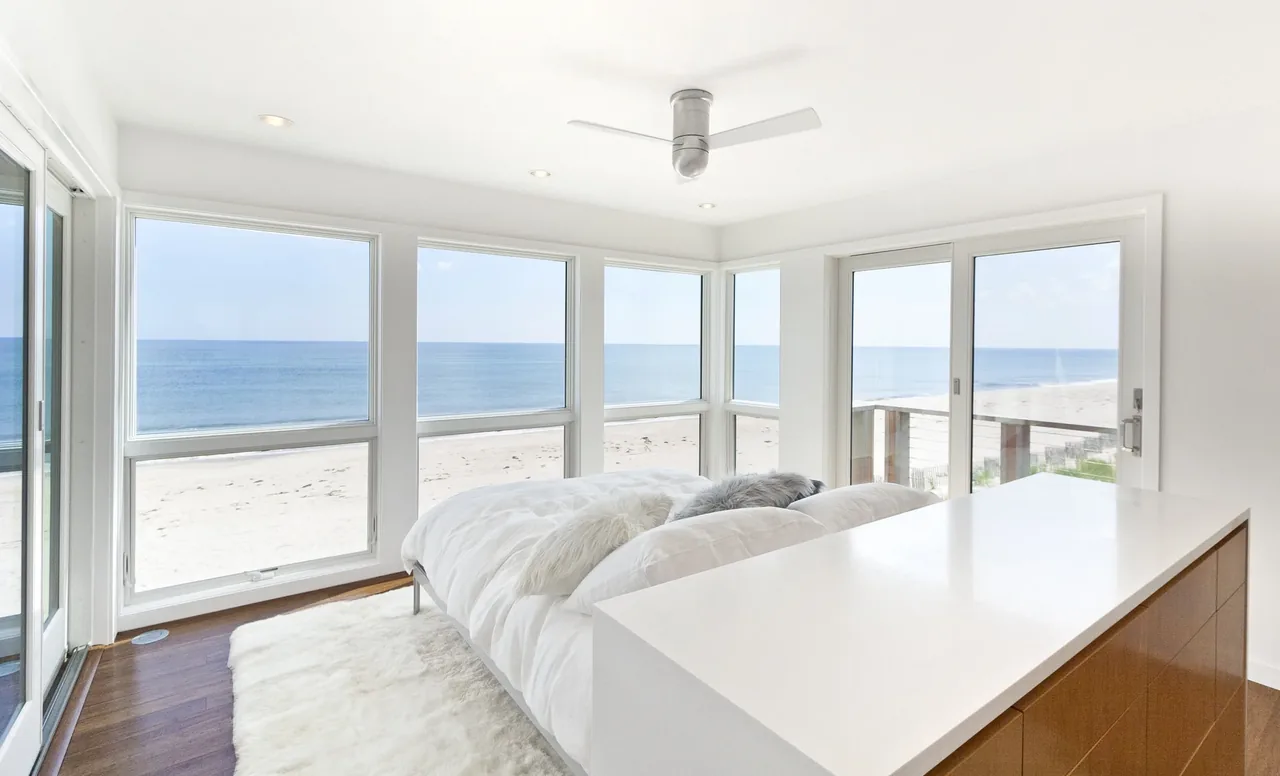 Beachfront bedroom with floor-to-ceiling windows offering expansive ocean views.