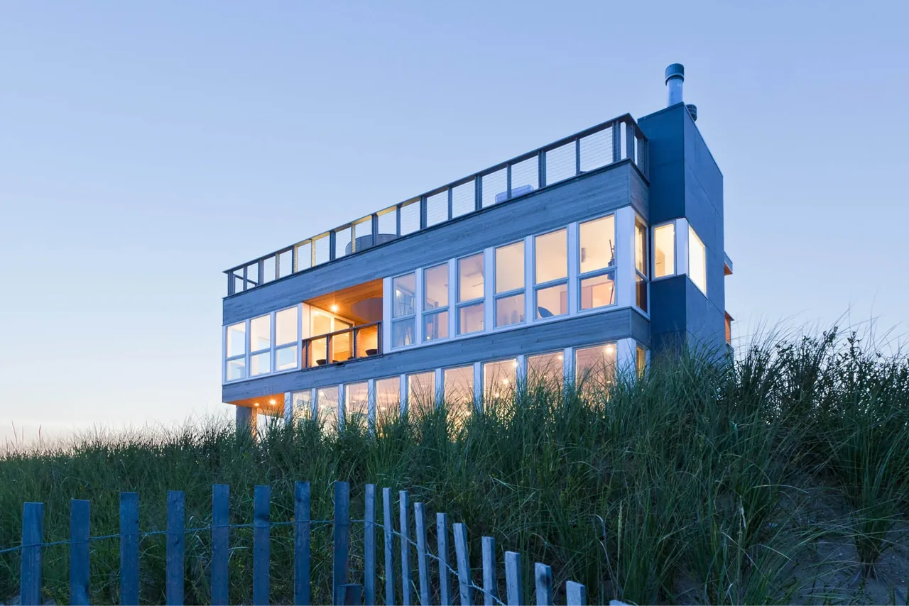 Dune Road Beach House in East Quogue, NY features extensive glazing and a rooftop deck with cable railings.