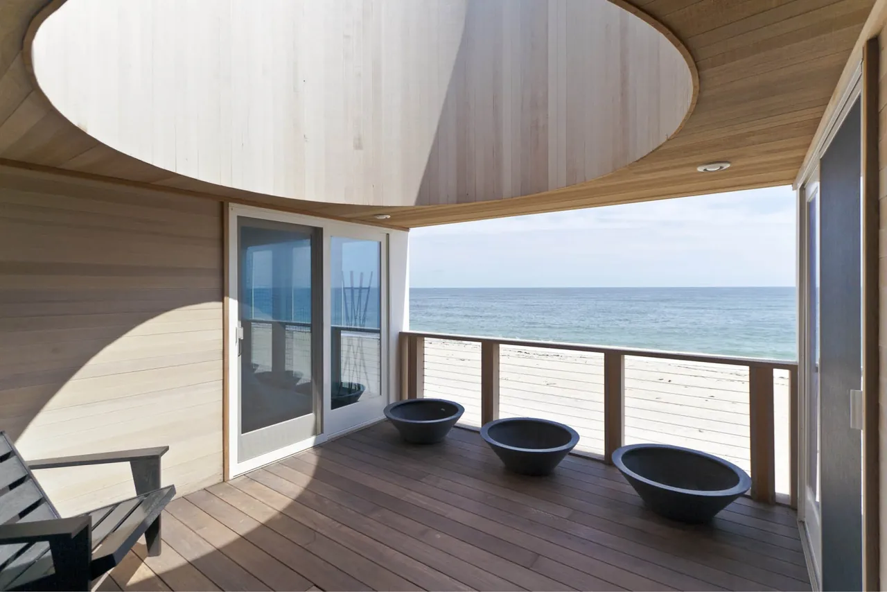Covered patio with circular ceiling detail and glass railing framing the ocean view at a beach house.