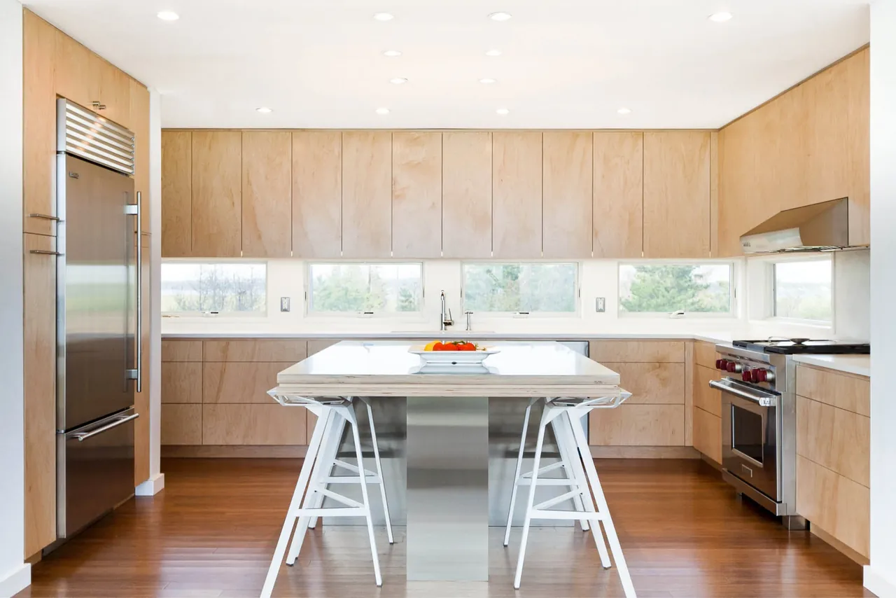 Kitchen with light wood cabinets, a stainless steel refrigerator, gas range, and a central island with white stools.