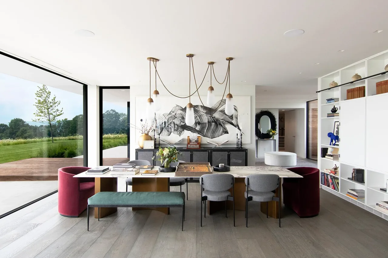 Dining room of the Millbrook Residence features a marble dining table, mixed seating, pendant lighting, and floor-to-ceiling windows.