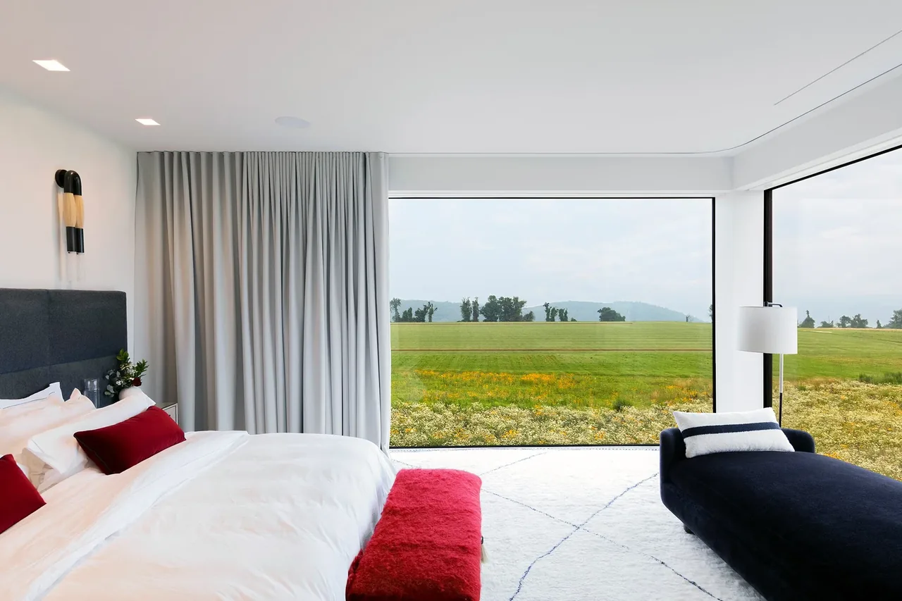 Modern bedroom features large corner windows offering expansive views of the green landscape outside.