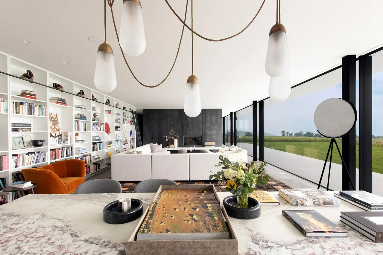 Living room and dining area of the Millbrook Residence feature floor-to-ceiling glazing and built-in shelving by Resolution 4 Architecture.