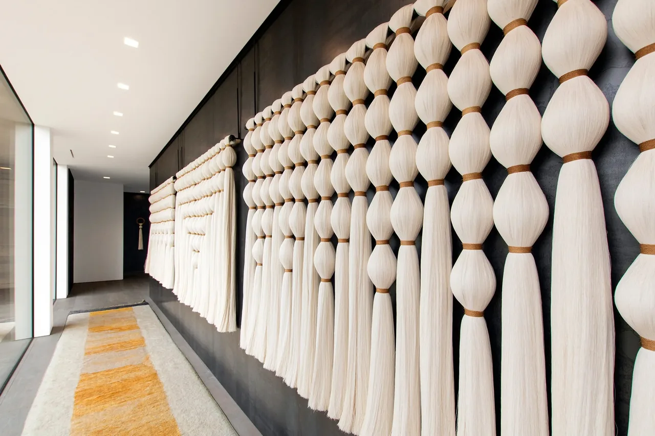 Hallway with dark walls showcases a large wall installation made of knotted white textile elements along one side.