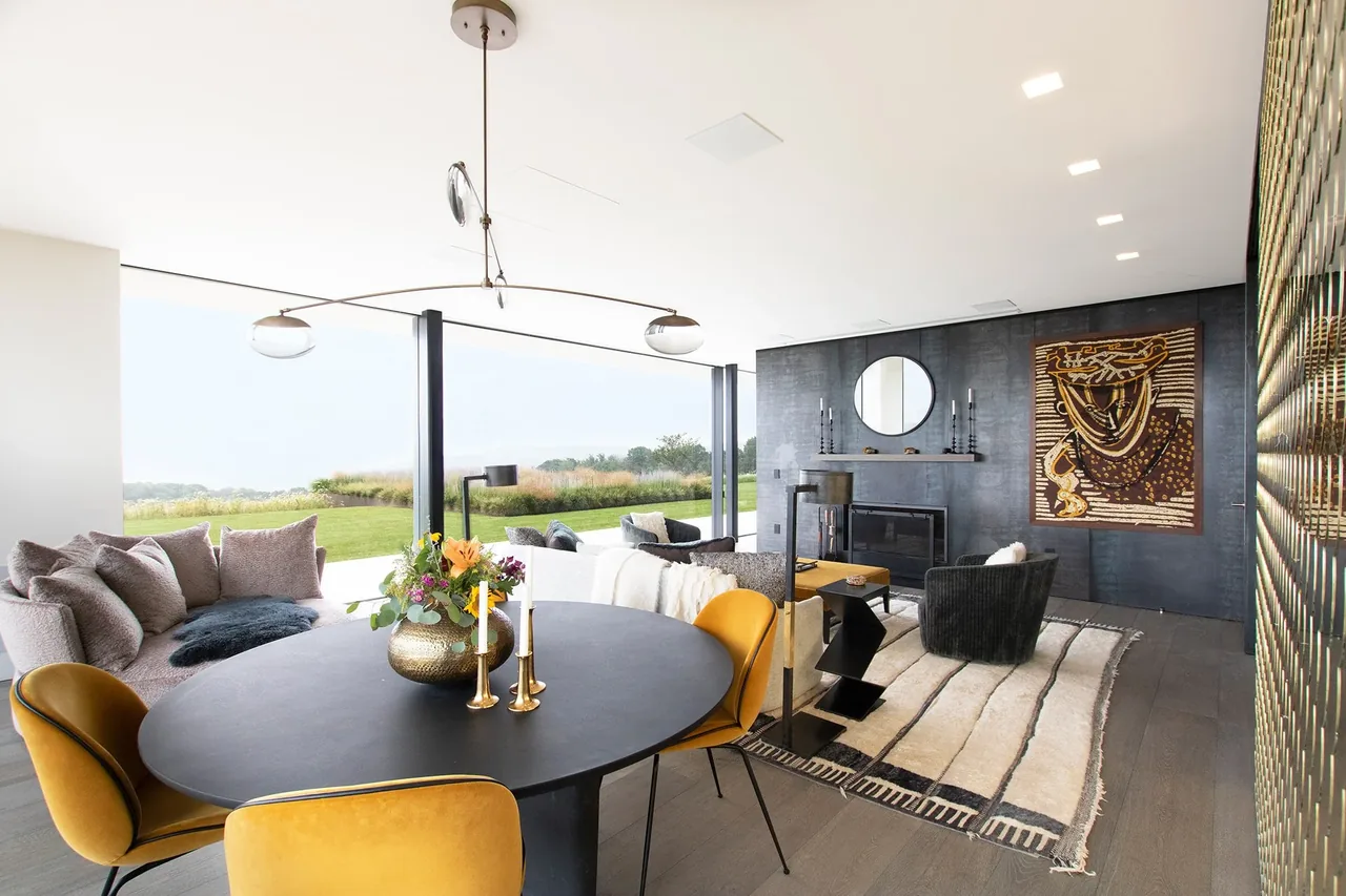 Open living and dining space with yellow seating, textile wall art, and large windows revealing an expansive meadow view at Millbrook Residence.