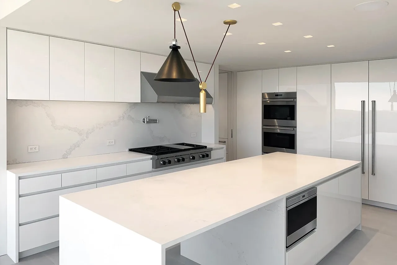 The kitchen features a large white island, built-in ovens, and black cone pendant lights over the counter area.