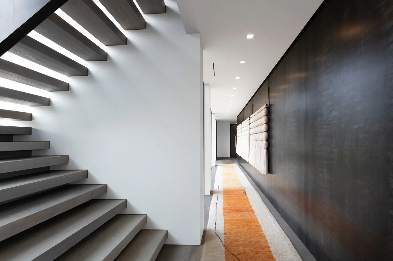 Float-style staircase adjacent to a hallway featuring a dark wall adorned with fabric art hanging and a narrow rug.