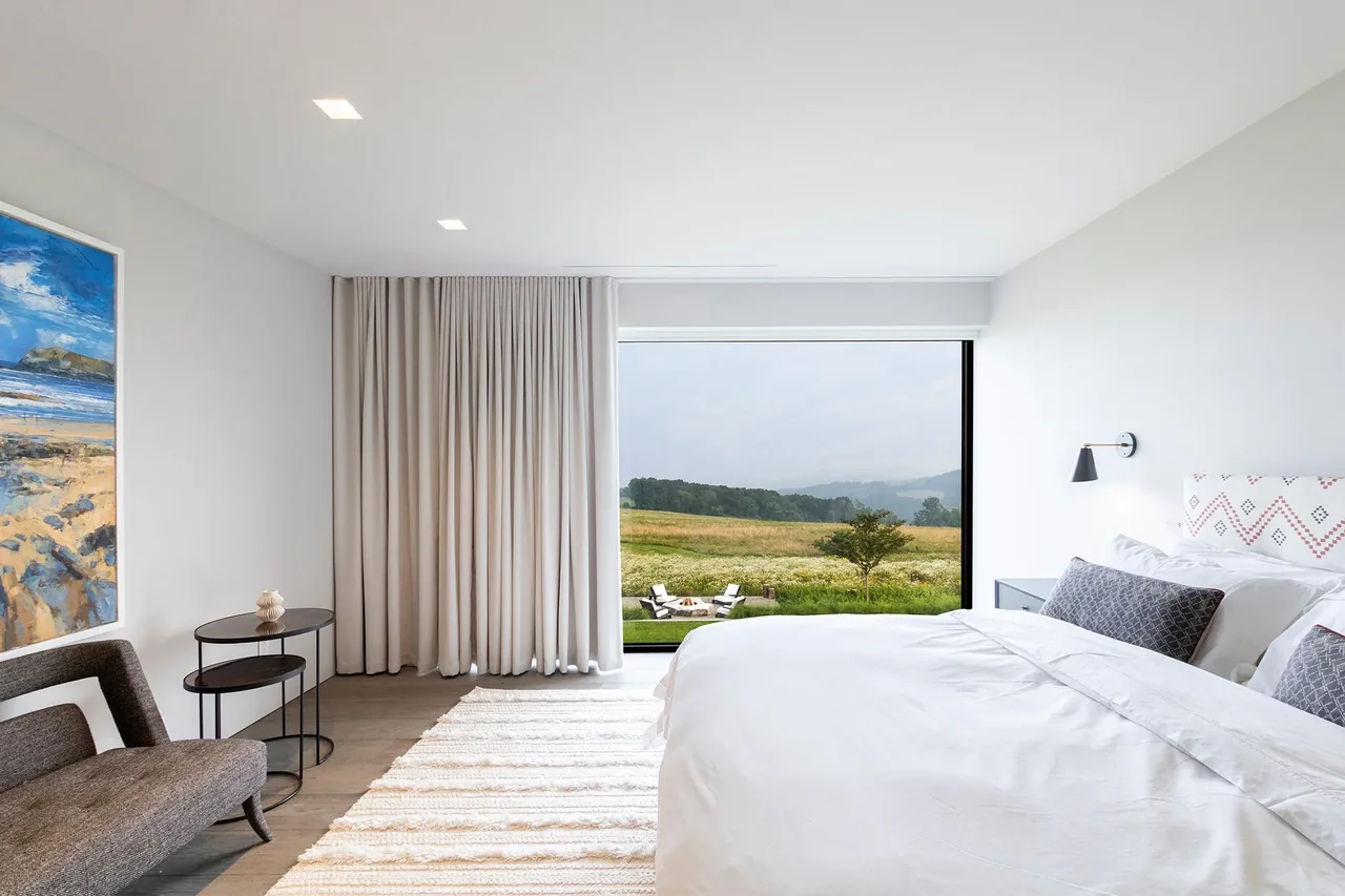 The bedroom of the Millbrook Residence features a large picture window framing the outdoor landscape in Dutchess County, NY.
