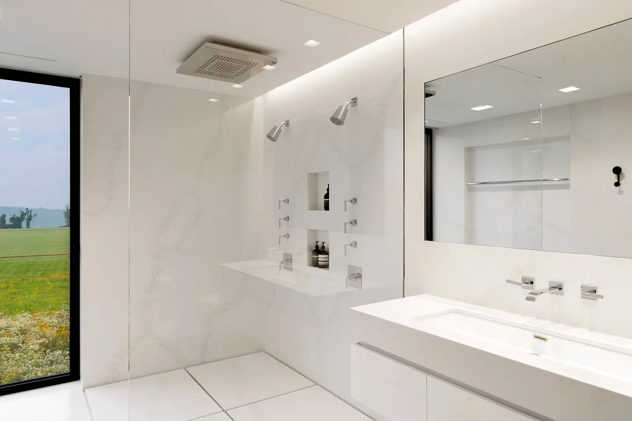 Millbrook Residence bathroom features a white double vanity, dual shower heads, and a large window with a view of the landscape.