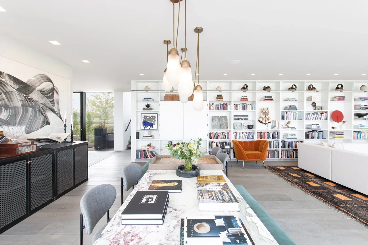 Interior view of the Millbrook Residence showing an open living and dining room with a marble dining table and wall-to-wall white shelving.