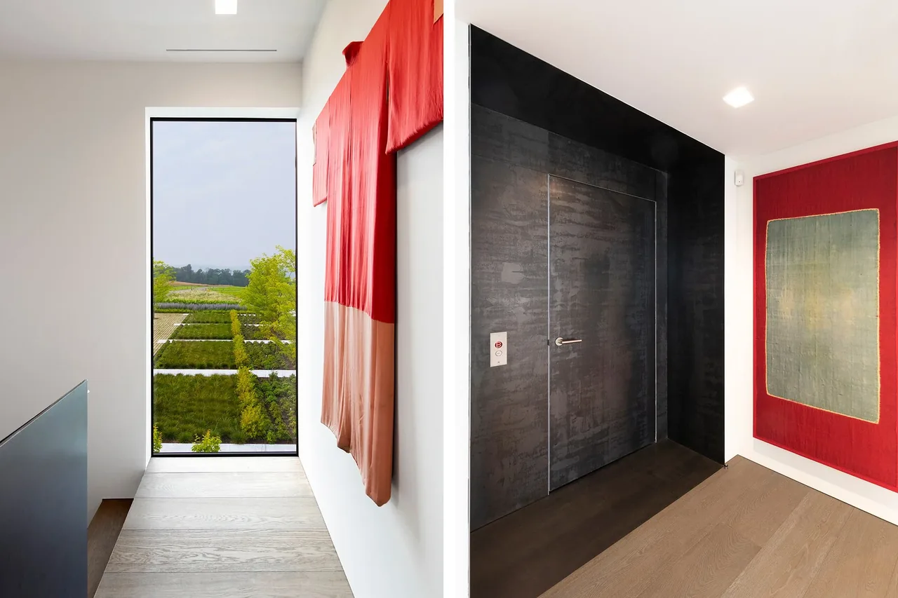 Hallway with floor-to-ceiling glazed window, black metal door, and colorful fabric wall art framing scenic landscape view.