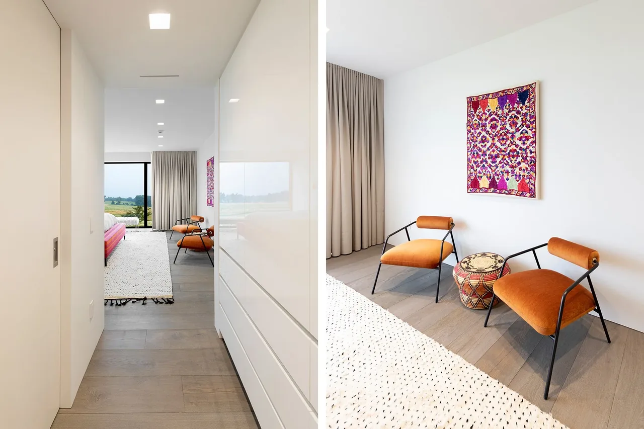 Millbrook Residence bedroom with orange chairs, fabric wall art, and large landscape window showing countryside view.