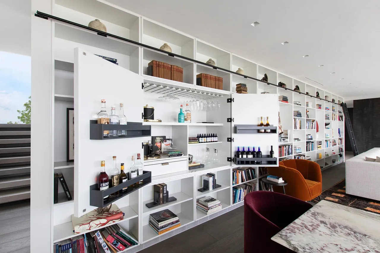 Living room features a built-in white bookshelf with a hidden bar cabinet, a white sectional sofa, and orange lounge chairs.