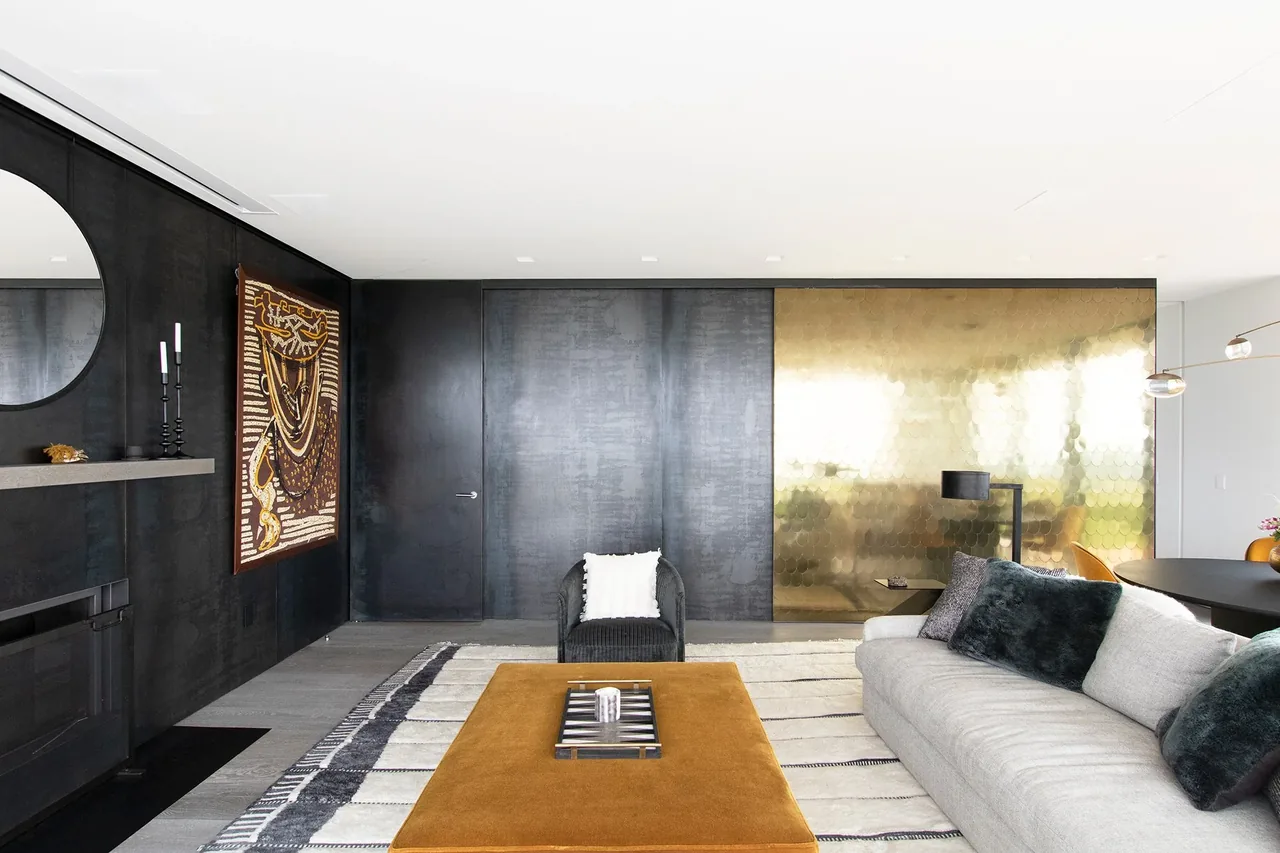 Living room of Millbrook Residence with dark walls, textile wall art, and a gold reflective panel.