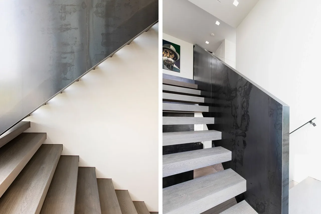 Floating gray wood stairs feature a blackened steel panel railing, illuminated by square skylights above.