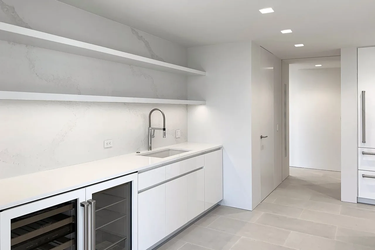 Kitchen space featuring white cabinets, marble backsplash, and a built-in wine fridge in the Millbrook Residence.