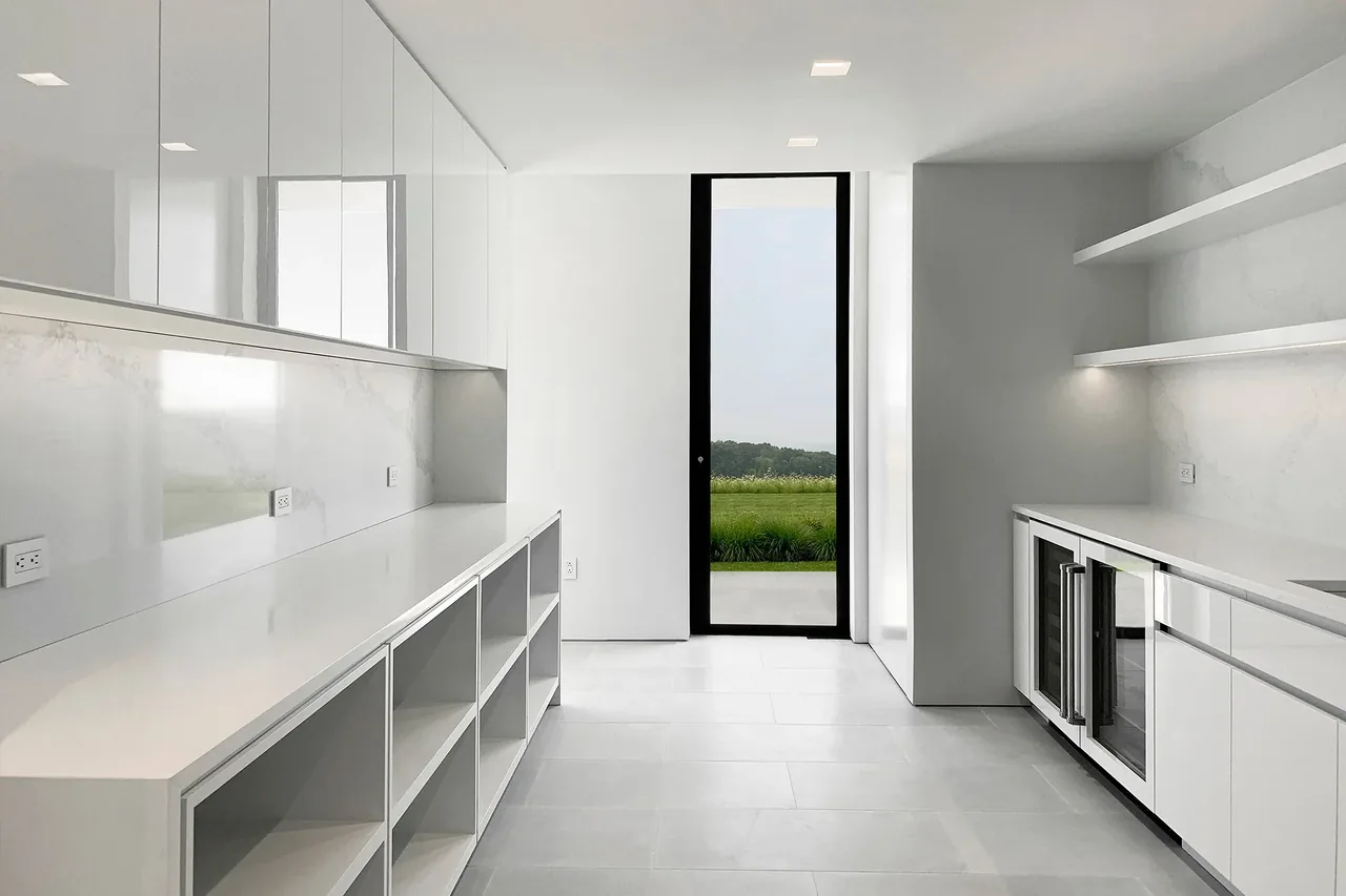 Modern kitchen features white cabinets, marble backsplash, and a glass door leading outdoors at Millbrook Residence.