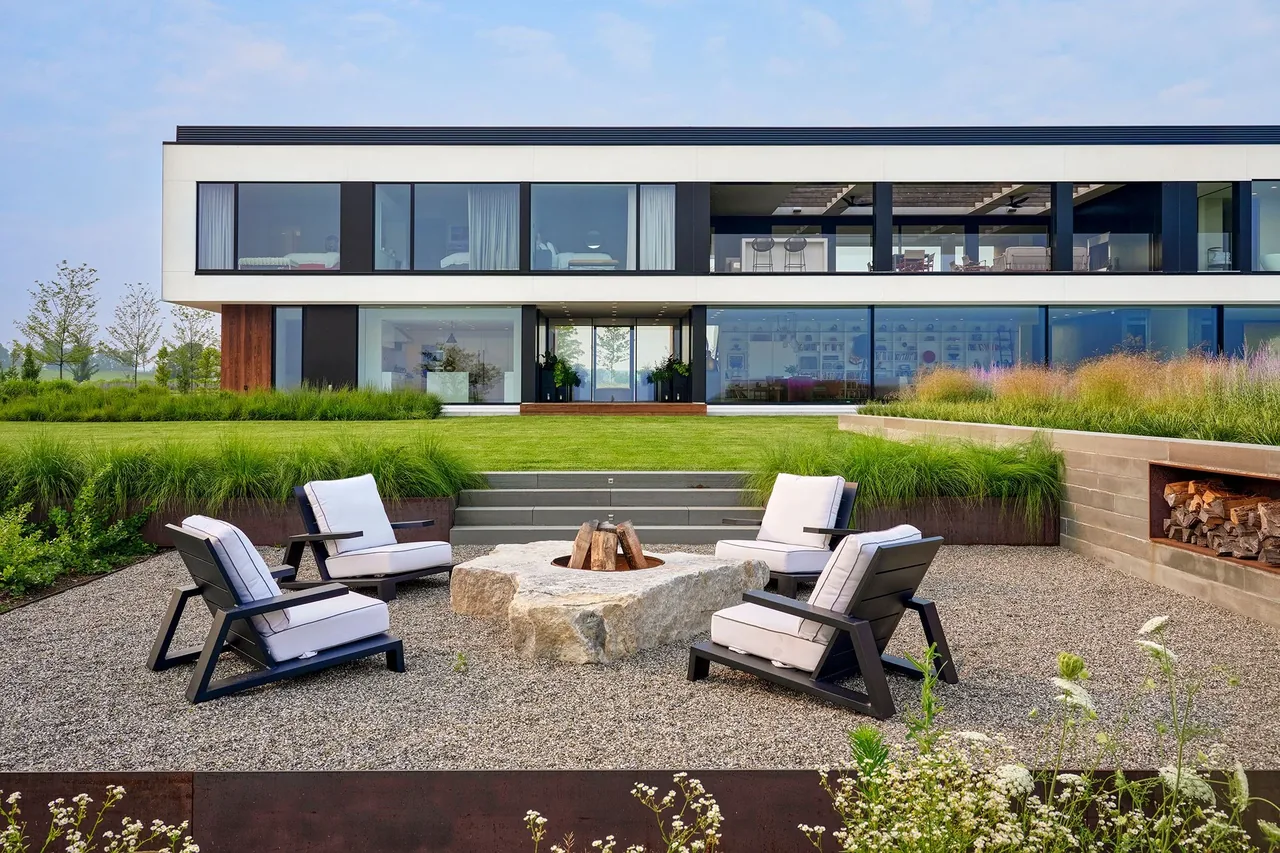 The Millbrook Residence features floor-to-ceiling glazing and a landscaped front yard with a stone firepit seating area.
