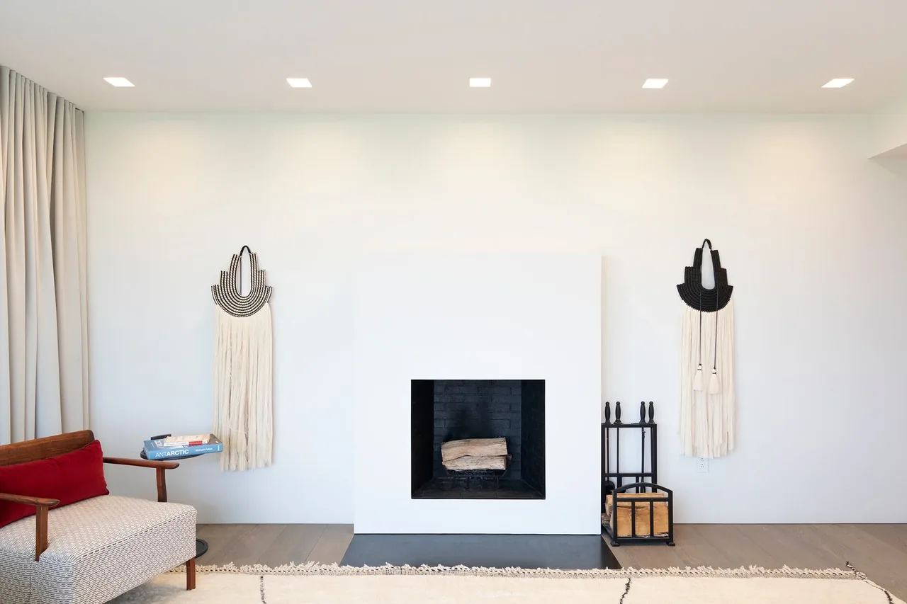 Living room with a white modern fireplace, fabric wall art, and a wooden chair with a red cushion.