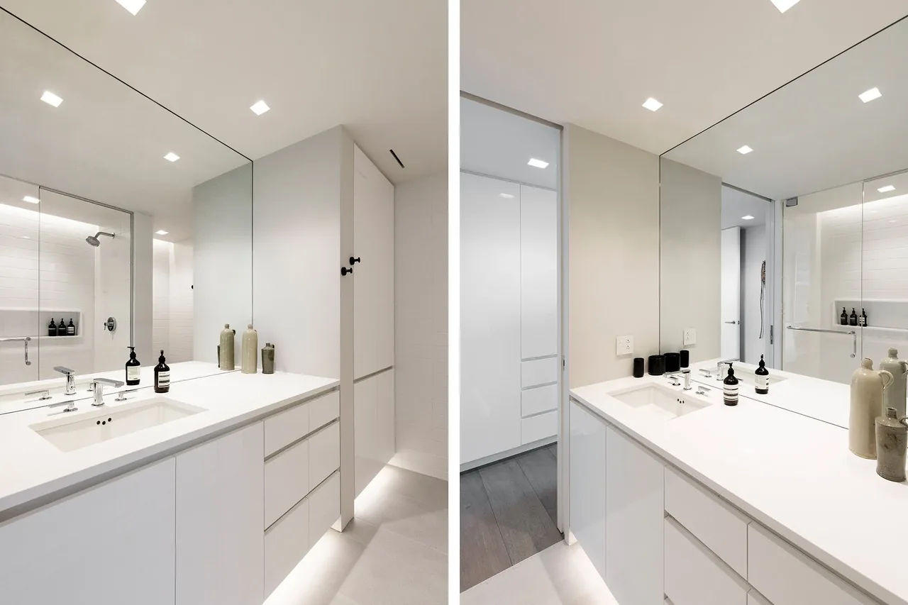 Minimalist bathroom featuring a large mirror, white vanity with undermount sink, and a walk-in shower with glass enclosure.