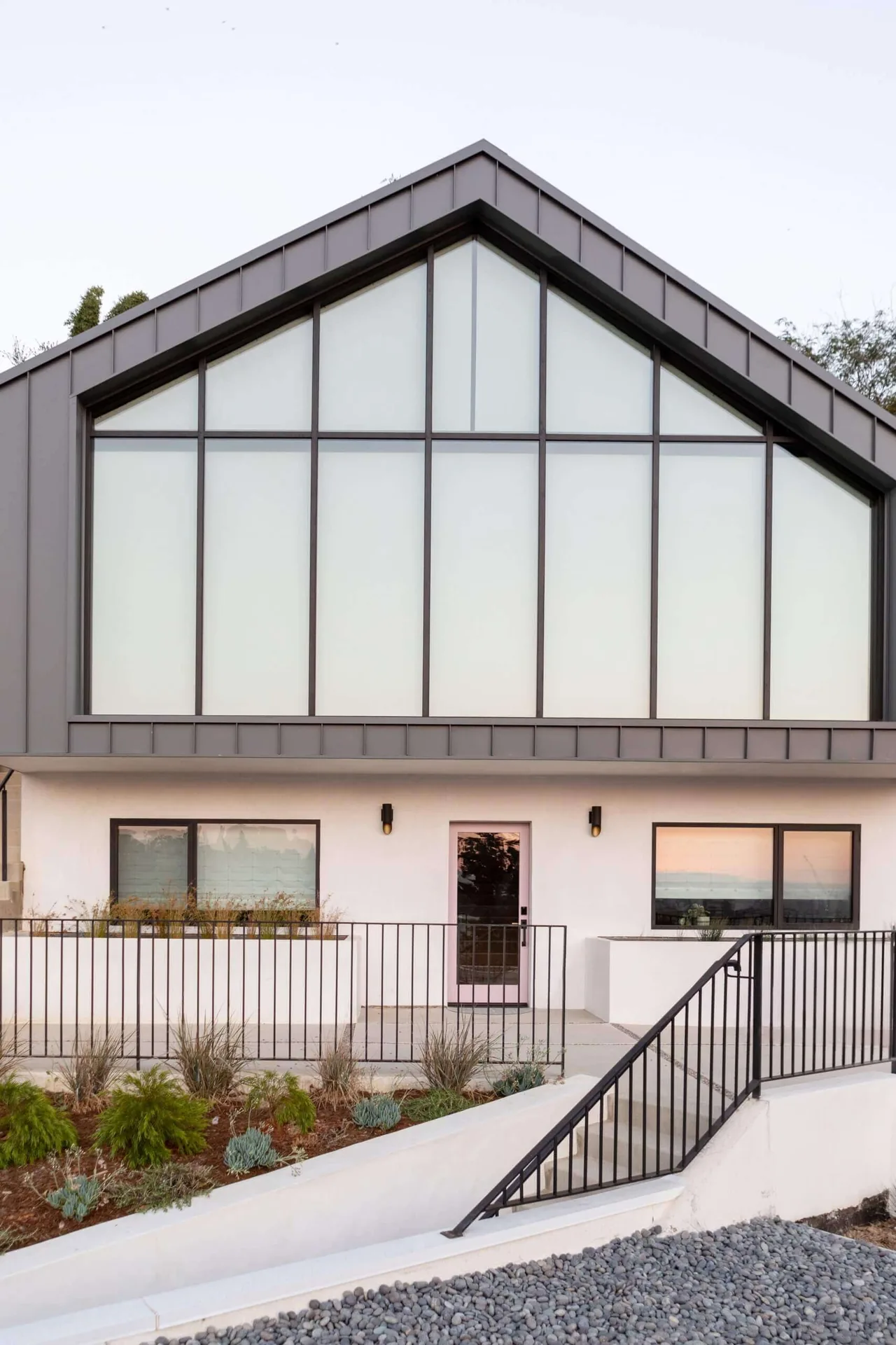 Hillside Home + Studio features a large frosted glass gable window and black metal railings in its exterior design.