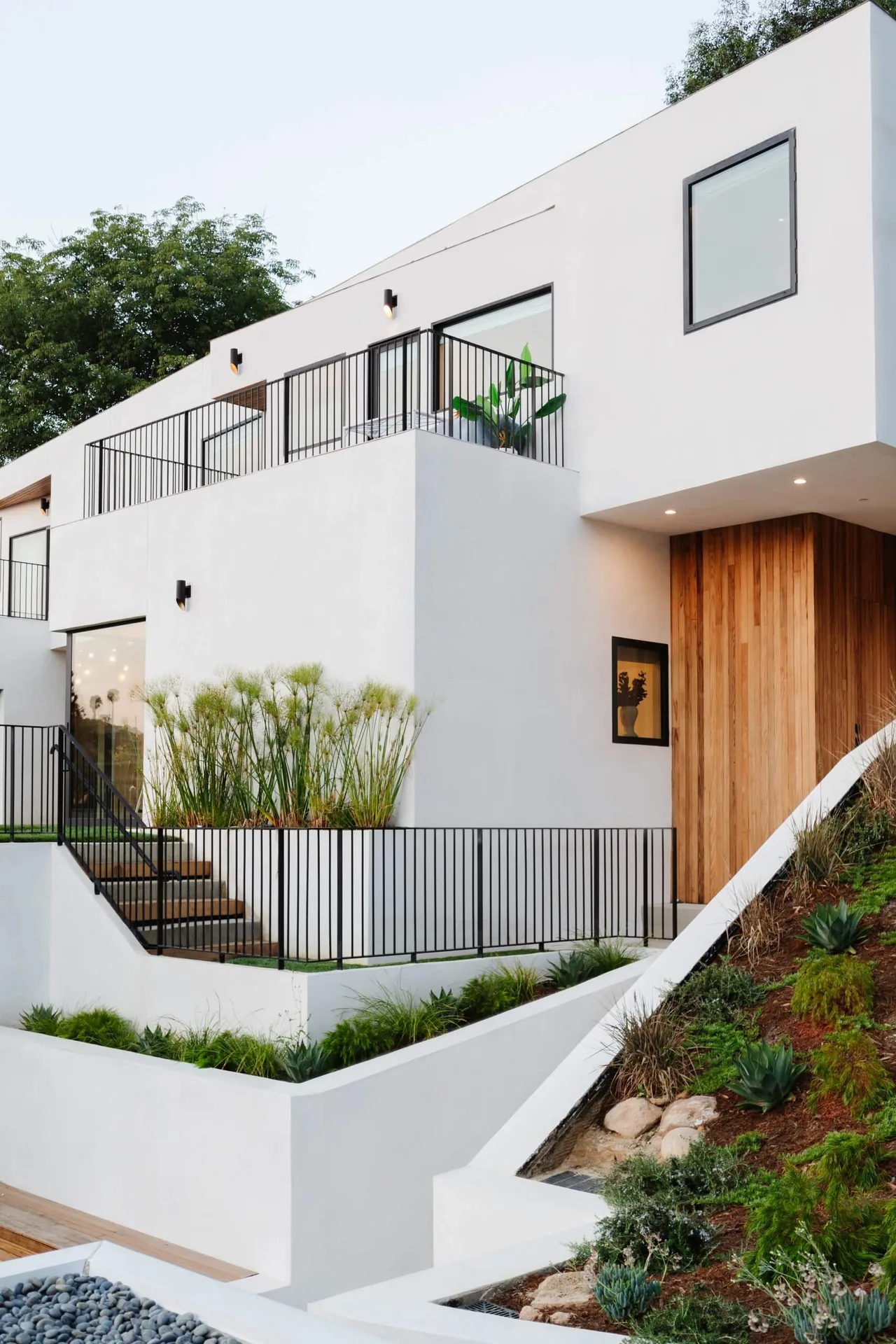 Hillside Home + Studio features clean white walls, black metal railings, and a wood-paneled front entrance.