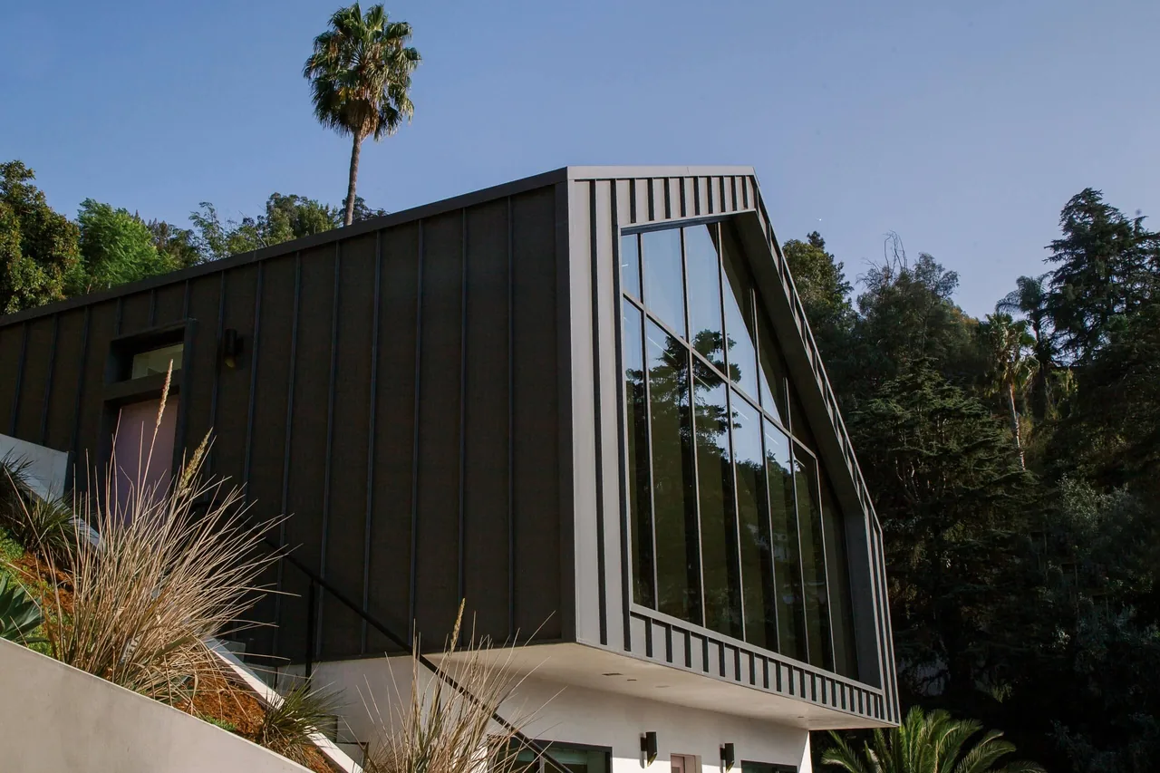 Hillside Home + Studio features a distinctive black vertical siding facade and large geometric window.