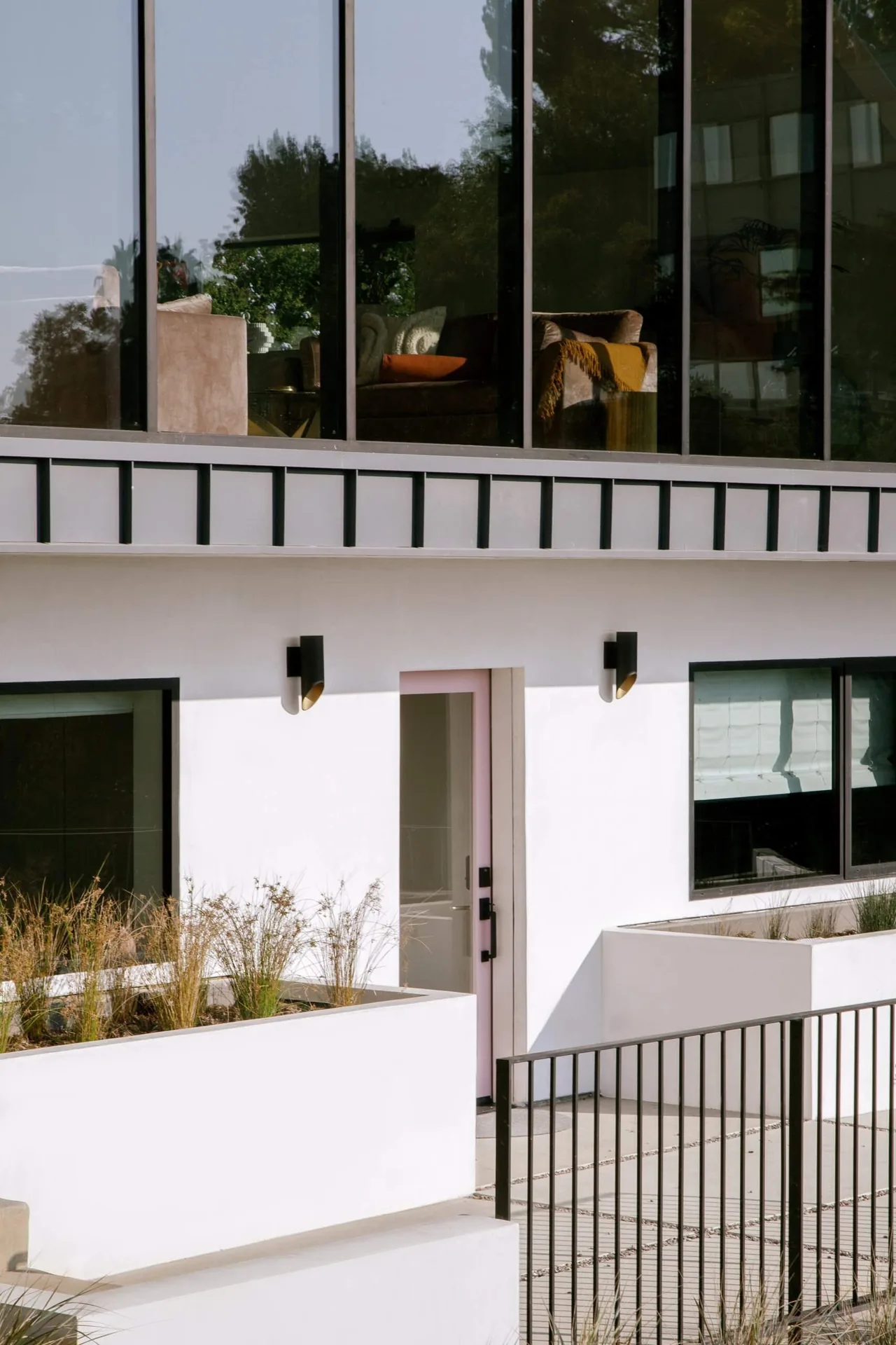 Hillside home exterior with large floor-to-ceiling windows, white stucco walls, and black metal railing.