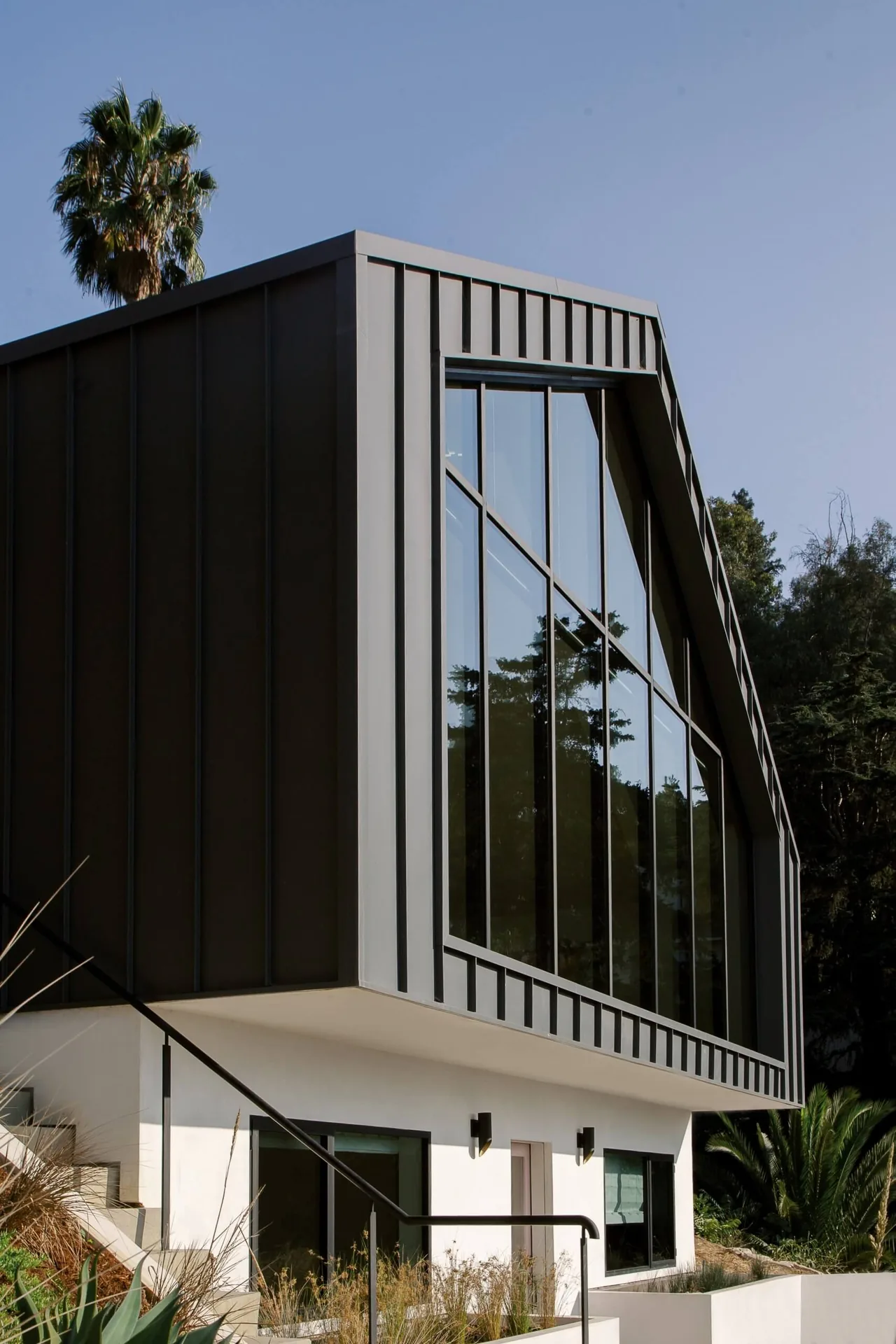 Hillside home with black metal vertical cladding and large floor-to-ceiling windows above a white stucco base.
