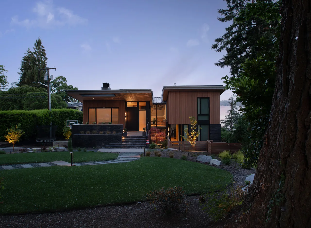 Wingspan Residence features flat roofs, wood siding, and an outdoor stair with metal railing, illuminated at dusk.