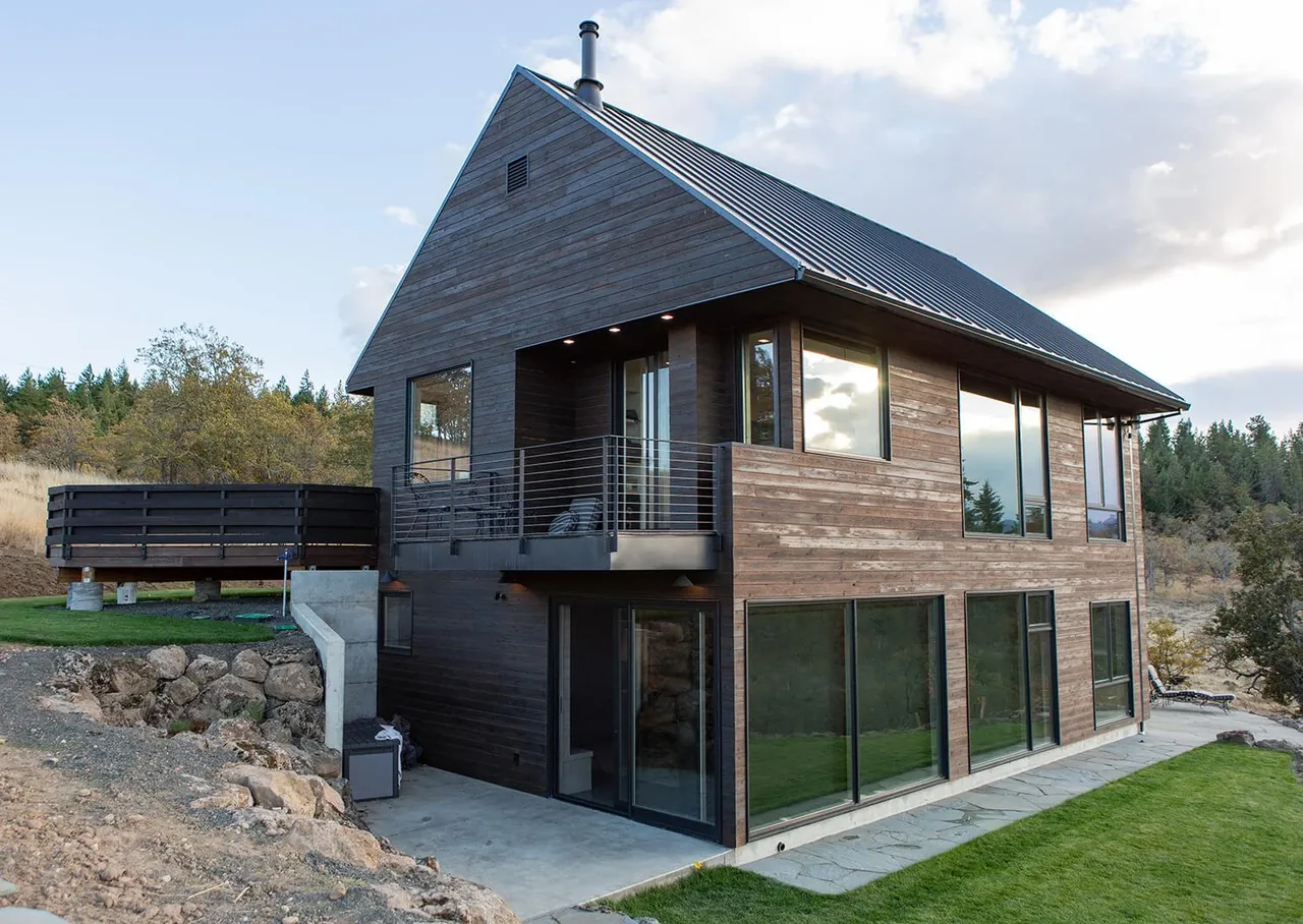 Mosier House features dark stained wood siding, a metal gable roof, and multiple large windows on two levels.