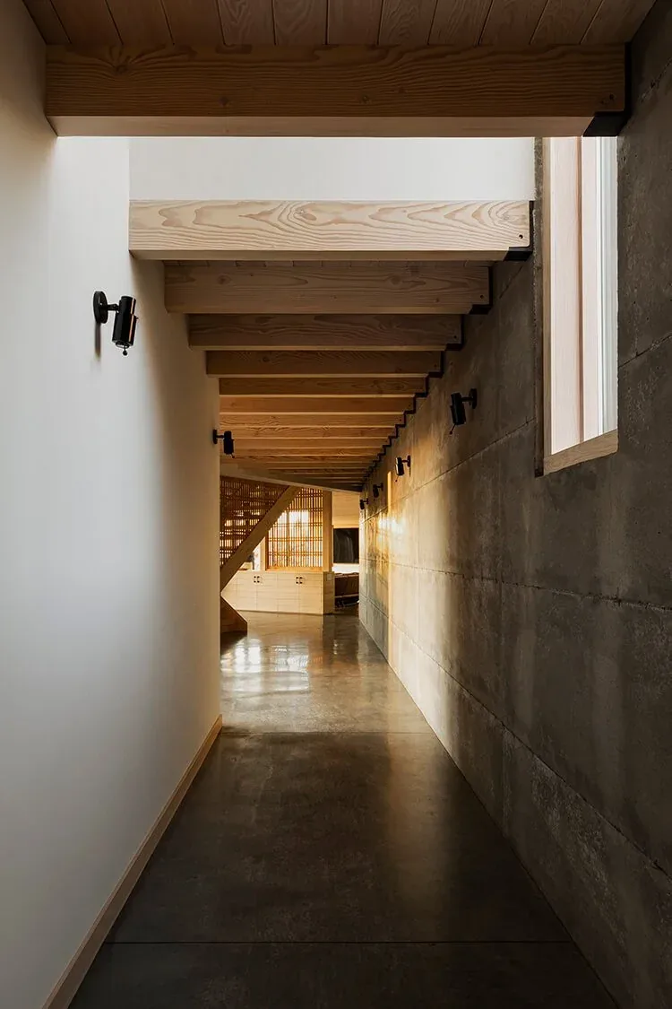 Mosier House hallway features exposed wood beams and concrete finishes with wall-mounted lights.