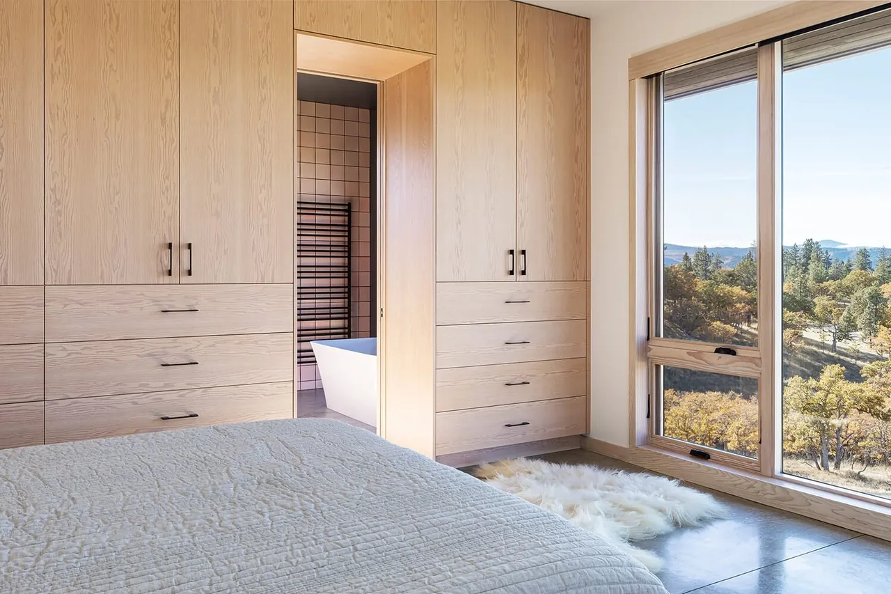 Bedroom features built-in light wood cabinetry and a large window with a scenic view of trees and hills outside.