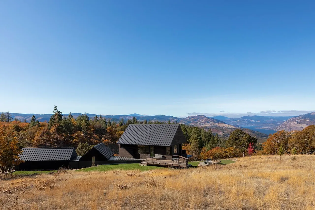 Mosier House by Richard Brown Architects features buildings with dark standing seam metal roofs on a grassy hillside with mountainous views.