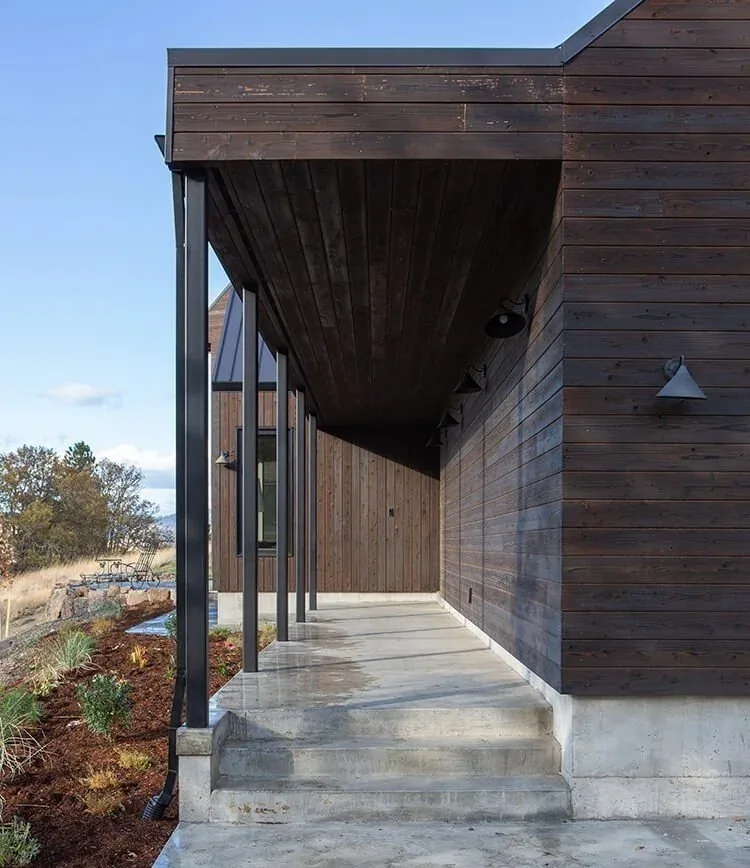 Walkway of Mosier House features dark wood siding and ceiling with polished concrete floor and steps.