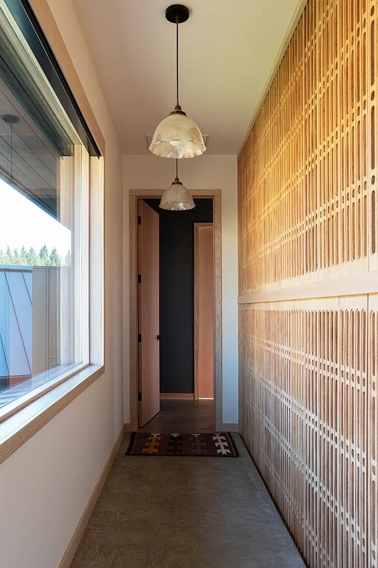 Interior hallway featuring a large window on one side and a wooden slatted wall on the other with pendant lighting.
