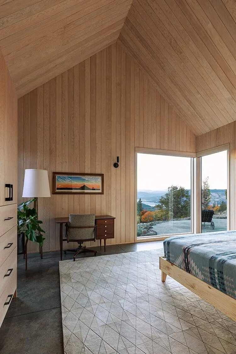 Mosier House bedroom features wood paneling and large corner windows framing scenic landscape views.