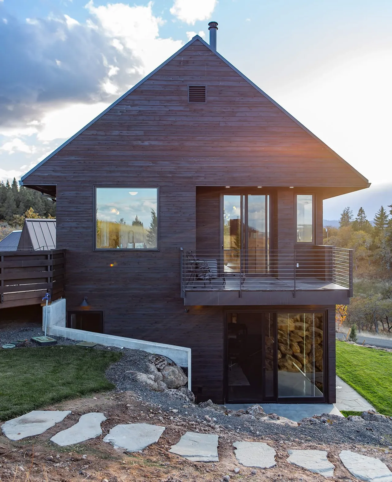 Mosier House by Richard Brown Architects features dark wood siding and a metal balcony overlooking a hillside landscape.