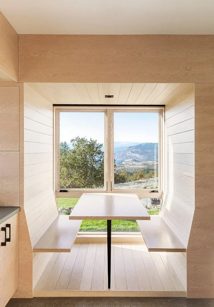 The Mosier House features a built-in dining nook with integrated wood benches and table framed by a large window with mountain views.