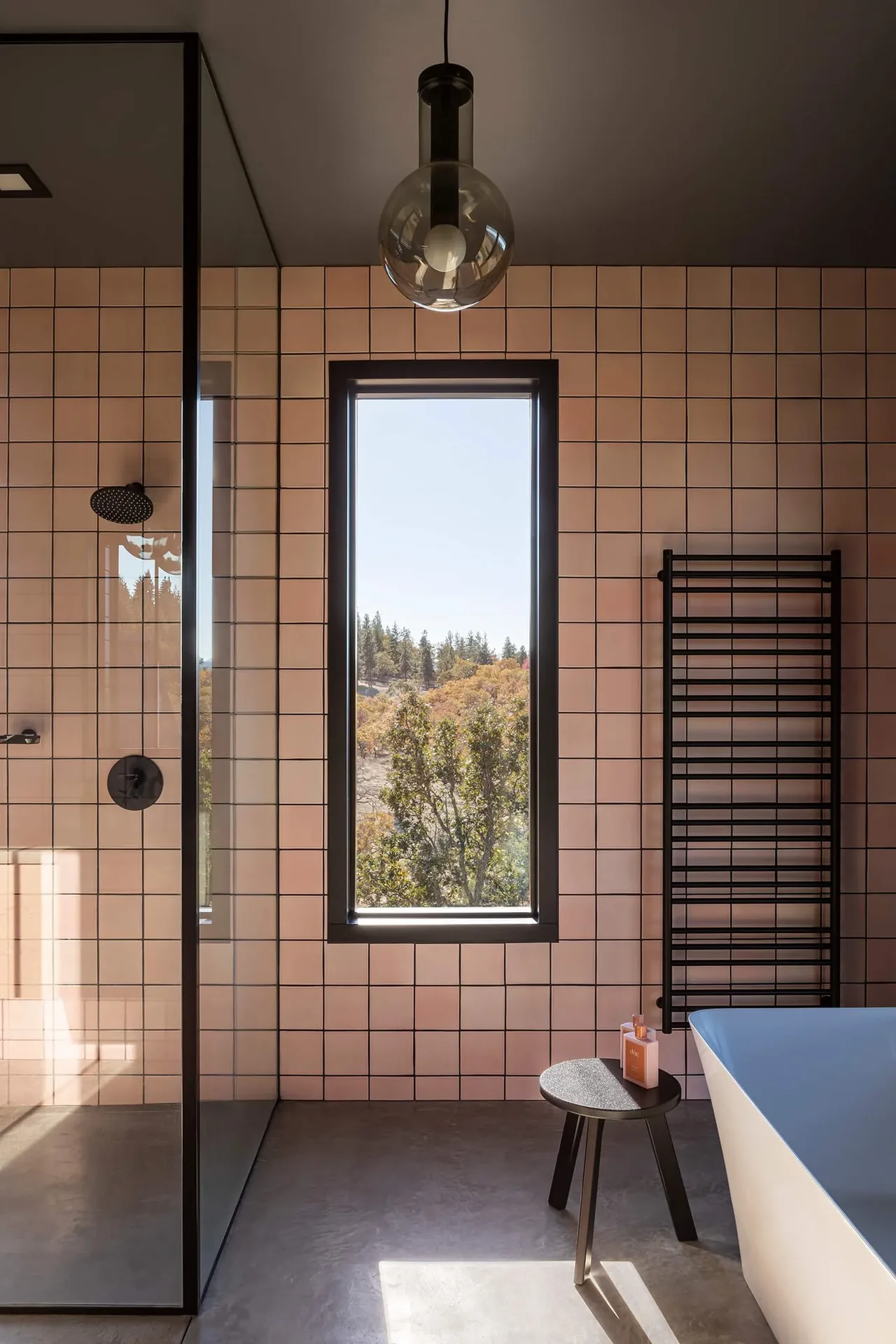Bathroom features peach square tiles, a black-framed window with a landscape view, and a black towel radiator next to a white bathtub.