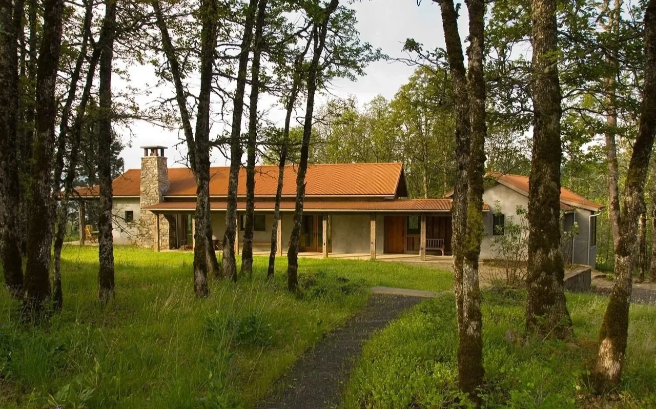 Columbia Gorge House features a metal gable roof and stone chimney, surrounded by trees and grass.
