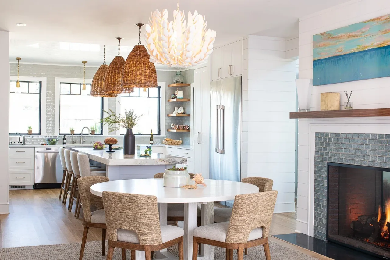 Open kitchen and dining space featuring a white round table, rattan chairs, and a fireplace with blue tile surround.