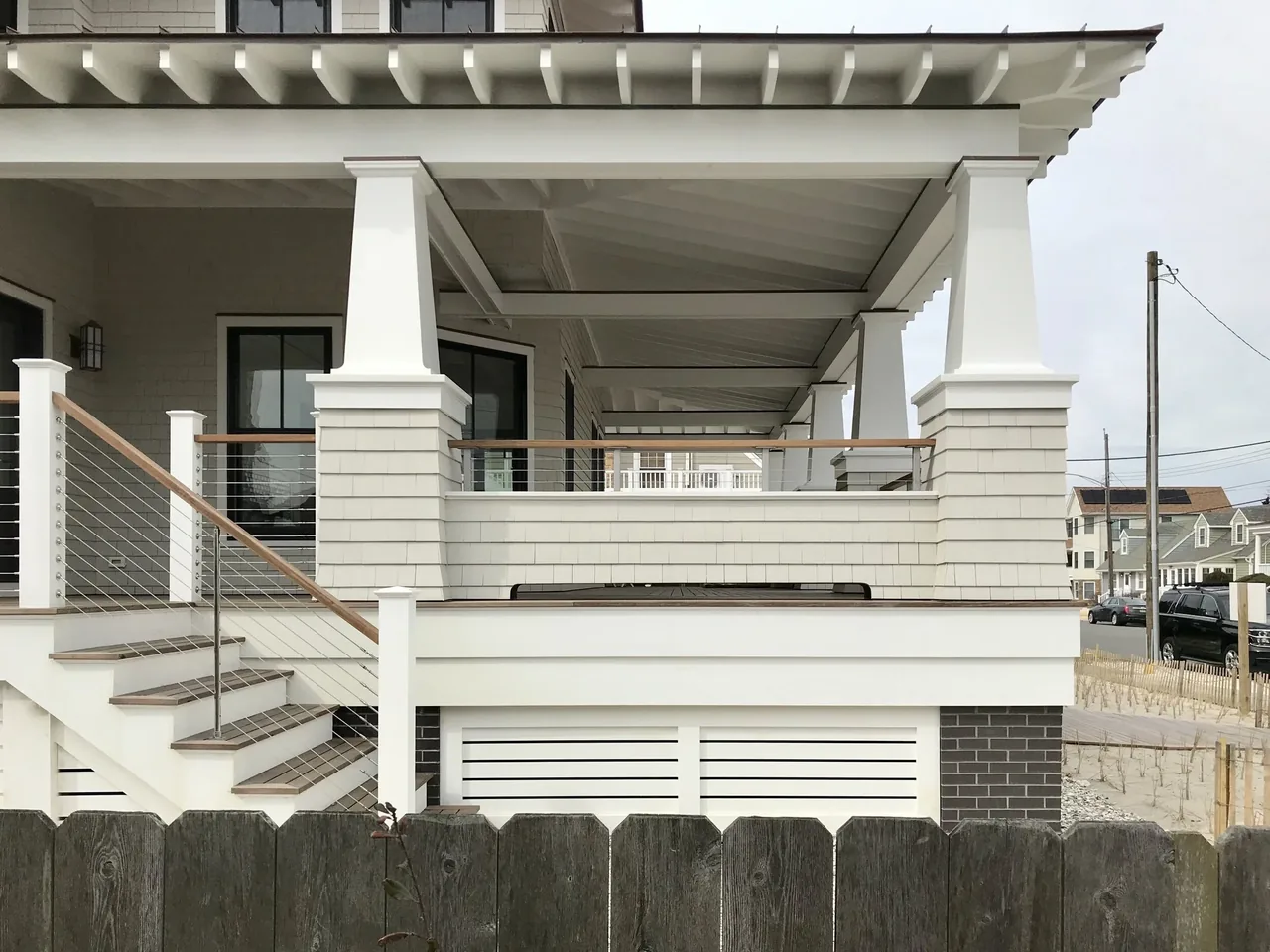 The Porch Talk House features a spacious wrap-around porch with tapered columns and cable railing, clad in white shingle siding.