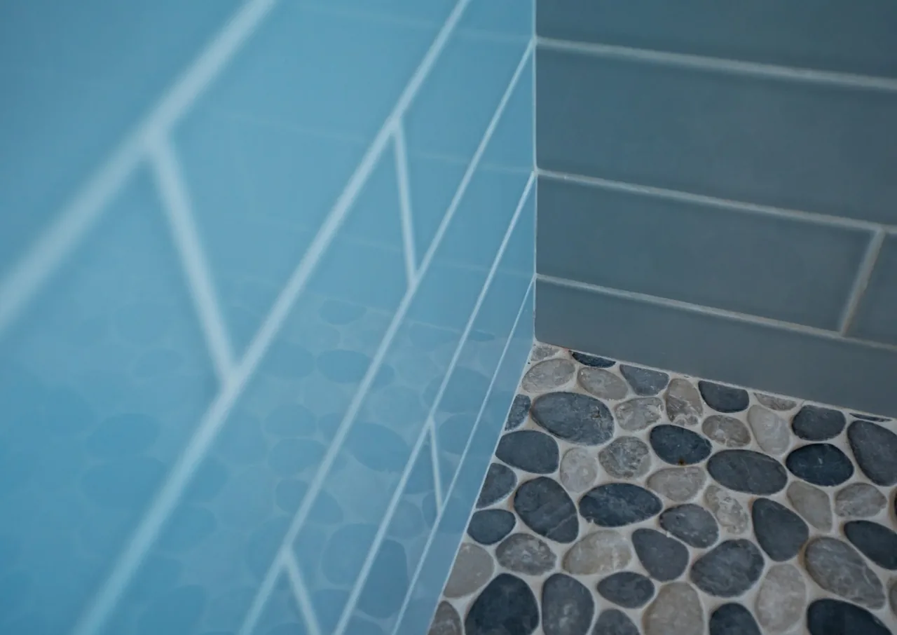 Corner detail of blue rectangular wall tiles with pebble stone floor tiles in the bathroom.