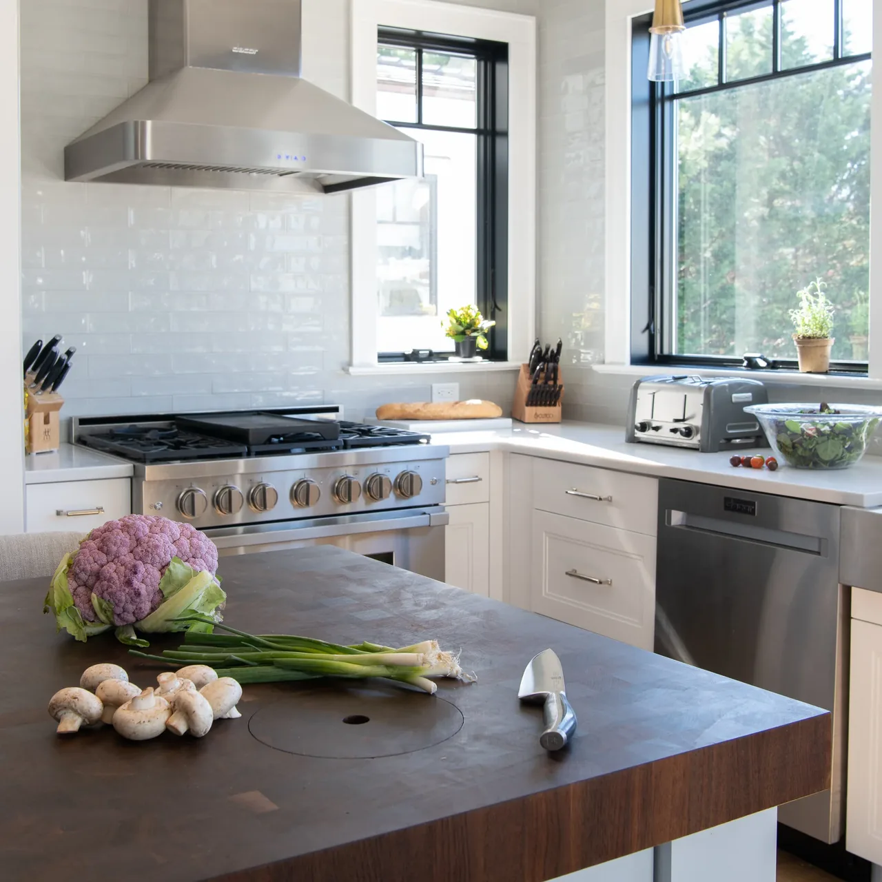 Kitchen featuring a wooden island, stainless steel gas range and dishwasher, white cabinetry, and black window frames.