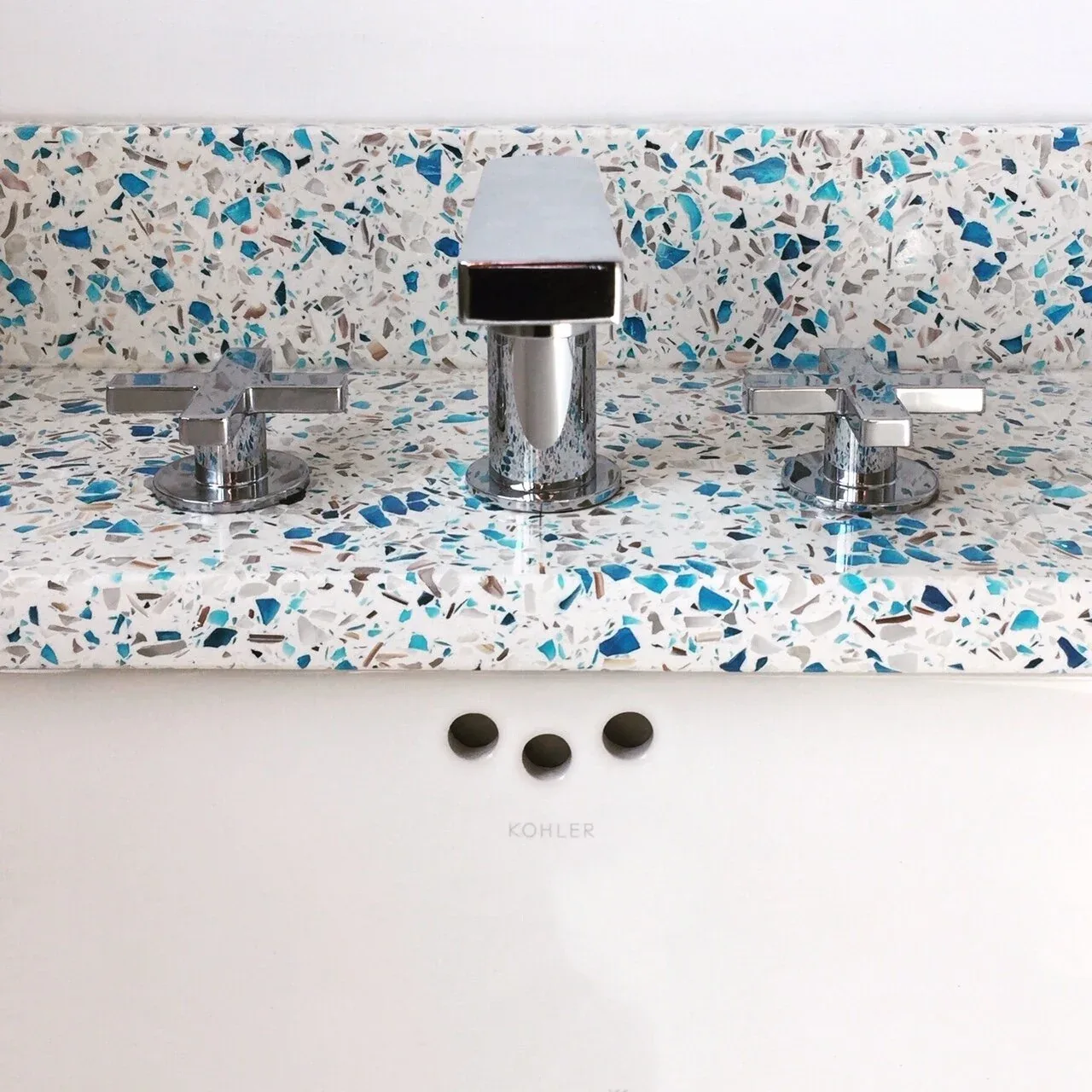 Modern chrome faucet and dual handles on a terrazzo bathroom countertop with blue and brown aggregates.
